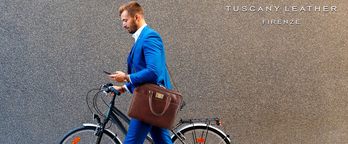 Man in a blue suit carrying a brown leather business bag beside a bicycle