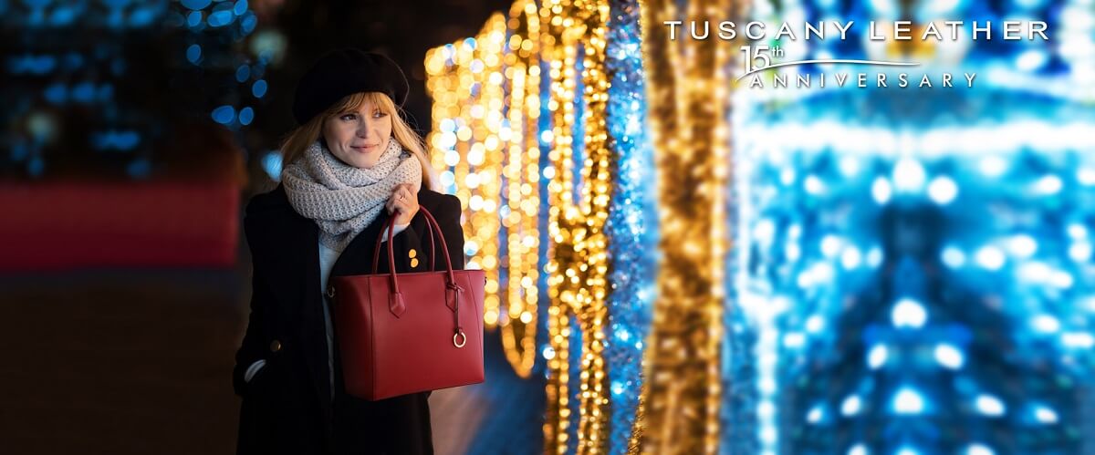 Woman in a black coat and grey scarf holding a red leather handbag beside decorative lights